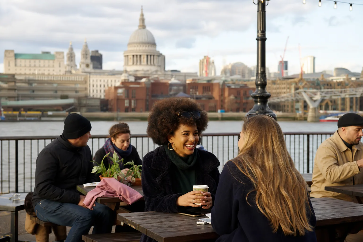 Two London singles sharing coffee on a bench beside the Thames